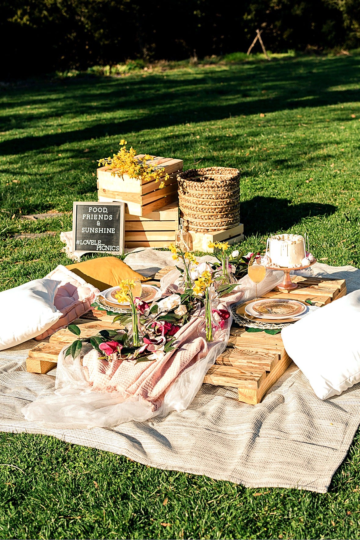 LoveLe Picnics sunny lawn setup — pallet table with flowers, cake on a stand and a Food Friends and Sunshine sign
