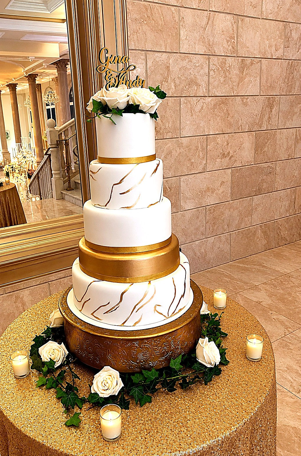 White and gold tiered Gina and Andy wedding cake with white roses on a gold stand