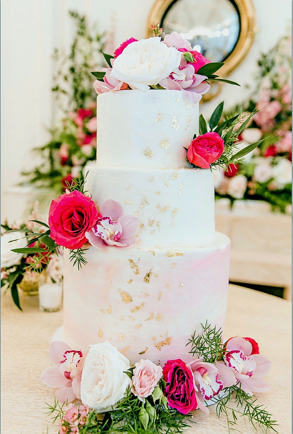 White and blush tiered wedding cake with gold leaf, pink roses and orchids